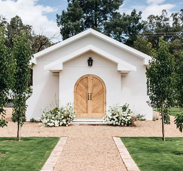 The Ballimore Church: white chapel with arched timber doors and white flowers either side